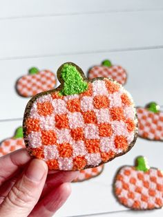 a hand holding up a decorated cookie with orange and white designs on the top, surrounded by small pumpkins