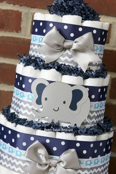 a three tiered baby shower cake with an elephant on the top and blue, white, and gray chevrons