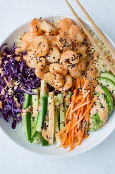 a white plate topped with shrimp, carrots and veggies next to chopsticks