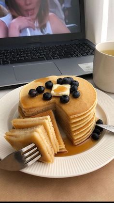 pancakes with blueberries and butter are on a plate next to a laptop