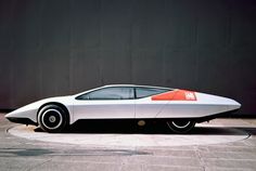 a futuristic car sitting on top of a cement floor next to a gray and orange wall