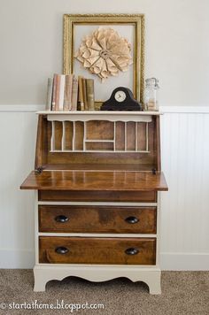 a wooden desk with drawers and a clock on top, in front of a white wall