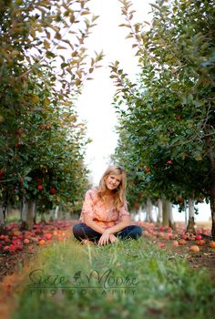 a woman sitting in the middle of an apple orchard