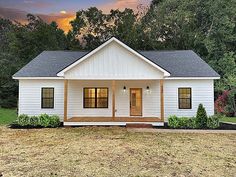 a small white house sitting on top of a grass covered field with trees in the background