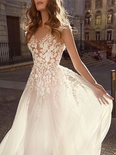 a woman in a white wedding dress standing on the street with her hand on her hip