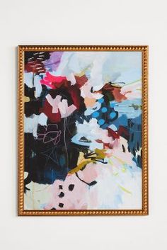 an abstract painting hangs on the wall in front of a white wall with gold frame