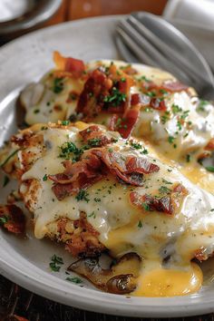 a white plate topped with cheesy potatoes covered in cheese and bacon next to a fork