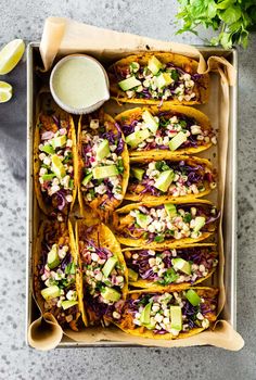 an overhead view of tacos in a box with salsa and avocado on the side