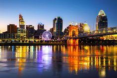 the city skyline is lit up at night with lights reflecting in the water and ferris wheel