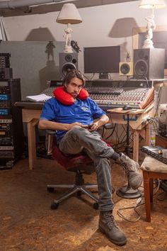 a man sitting in front of a mixing desk with headphones on his ears and holding a red pillow over his shoulder