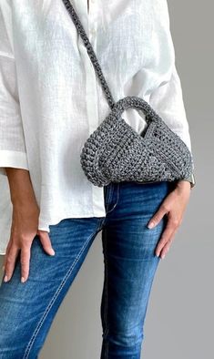 a woman wearing jeans and a white shirt is holding a crocheted handbag