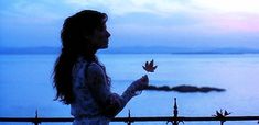 a woman standing next to a fence near the ocean