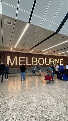 people walking through an airport with luggage and signs on the wall behind them that say melbourne