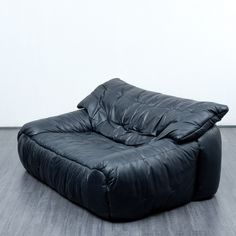 a large black leather chair sitting on top of a hard wood floor covered in white walls