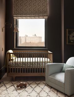 a baby's room with a crib, chair and window overlooking the city