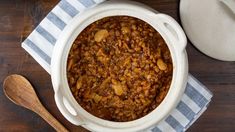 a white bowl filled with baked beans next to a wooden spoon on top of a table