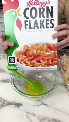 a person holding up a box of corn flakes next to a bowl of cereal