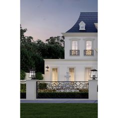 a large white house with a black iron fence and two lamps on the front porch