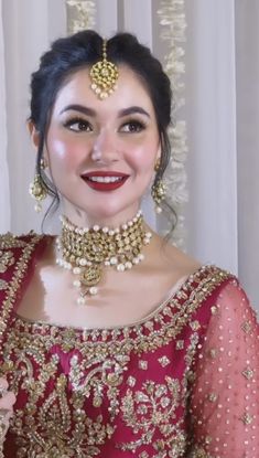 a woman in a red and gold outfit with jewelry on her head, smiling at the camera