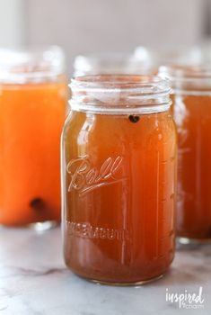 three jars filled with liquid sitting on top of a table next to apples and cinnamon sticks