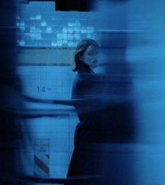 a blurry photo of a woman standing in a blue room with tiled walls and floor