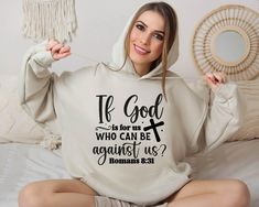 a woman sitting on a bed wearing a sweatshirt that says, if god is for us who can be against us?