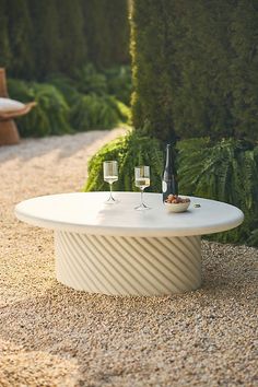 a table with two wine glasses on it in the middle of a gravel garden area