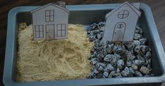 two houses made out of sand and gravel in a blue tray on a wooden table