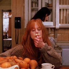 a woman sitting at a table with oranges in front of her and a coffee cup