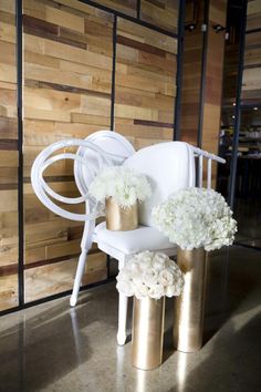 a white chair sitting next to two gold vases filled with flowers on top of stools