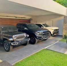 two pickup trucks parked in front of a modern home with garage doors open and grass on the driveway