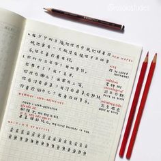 two red pencils sitting on top of an open book with chinese writing in it