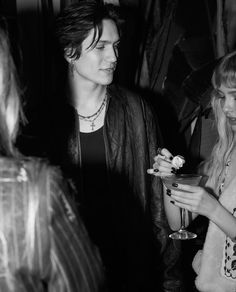 two women standing next to each other holding drinks in their hands and looking at something on the table