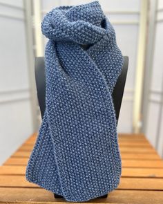 a blue knitted scarf sitting on top of a wooden table next to a chair