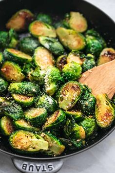 brussel sprouts are being cooked in a skillet with a wooden spoon