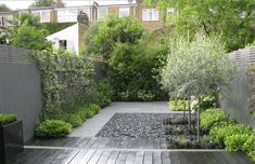 a wooden deck surrounded by trees and plants in a garden area with graveled walkway