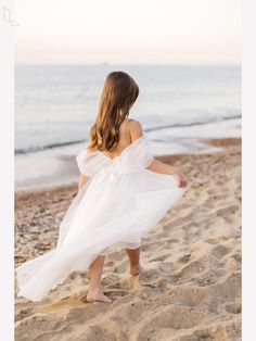 a woman standing on top of a sandy beach next to the ocean wearing a white dress