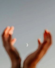 a hand reaching up to the sky with a half moon in the distance behind it