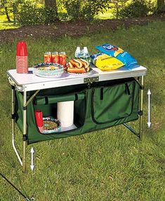 a picnic table with food and drinks on it in the grass next to some trees