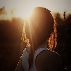 a woman standing in front of the sun with her back turned to the camera and looking into the distance