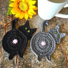 two crocheted cats sitting next to a coffee cup on top of a table