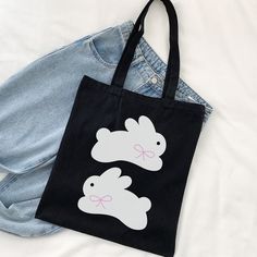 a black bag with two white rabbits on it sitting next to a pair of jeans