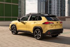 the rear end of a yellow suv parked in front of tall buildings