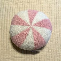 a pink and white striped round cushion sitting on top of a beige tablecloth covered floor