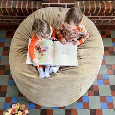 two children sitting on a bean bag chair reading a book