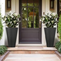 two large black planters with white flowers in front of a door