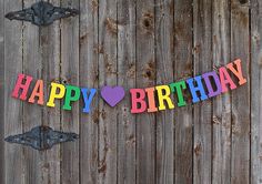 a happy birthday banner hanging on a wooden fence with an arrow and heart in the center