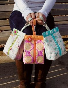 a woman sitting on a bench holding three purses in her hands, both with zippered handles