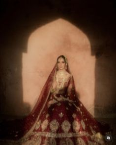 a woman in a red and gold wedding dress sitting on the floor with her hands behind her back