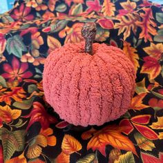 a pink crocheted pumpkin sitting on top of a floral tablecloth with leaves